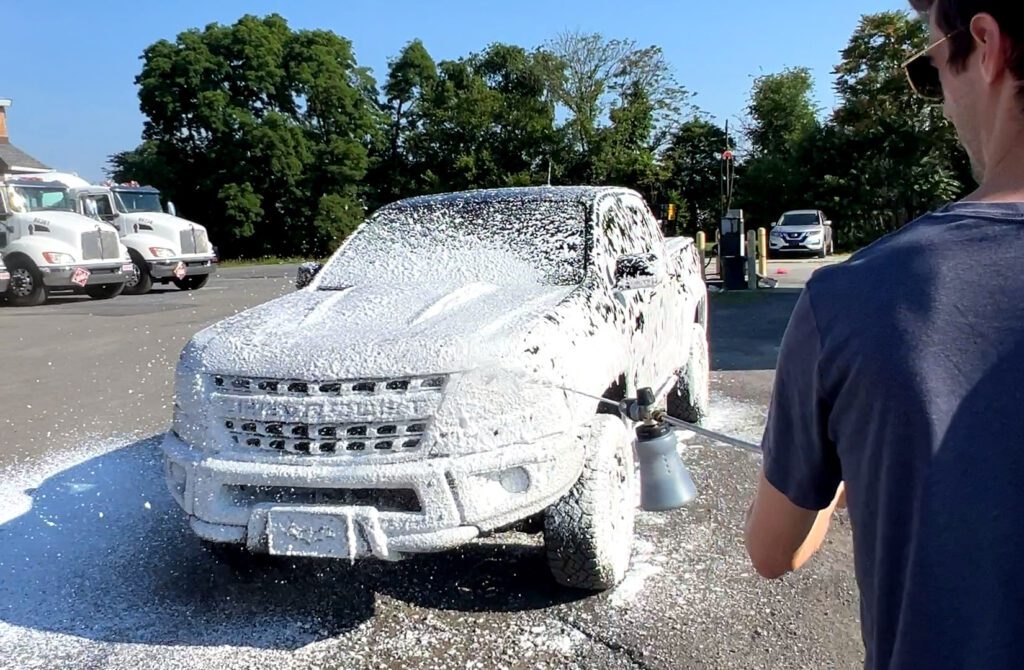 Using a foam cannon to apply snow foam to a truck.
