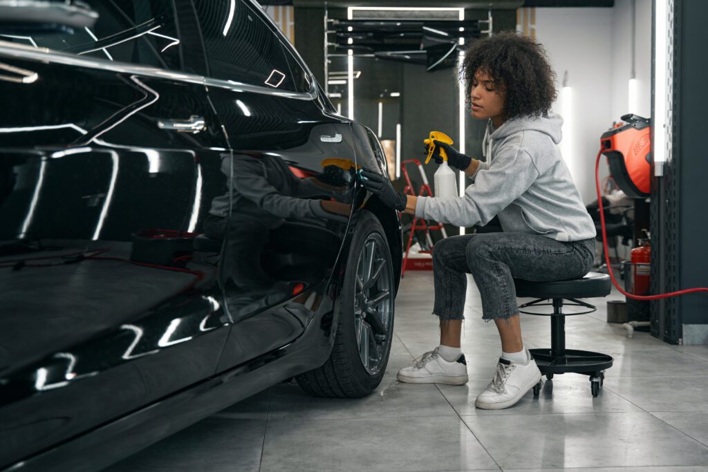 Detailer clays a car while sitting on a comfortable stool.