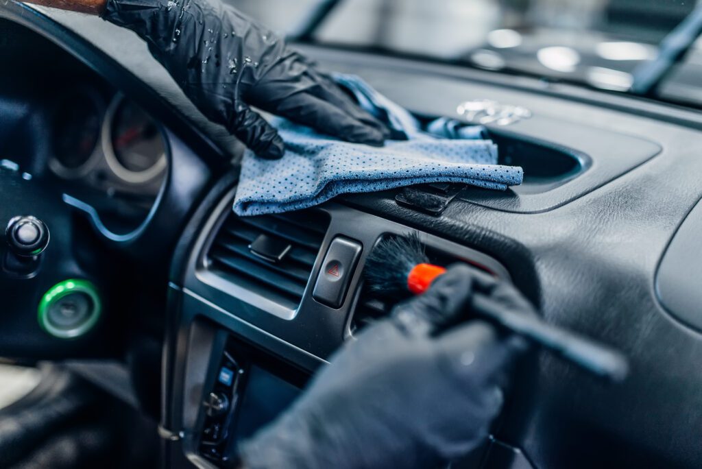 A detailer uses a brush to clean a car's air vents.