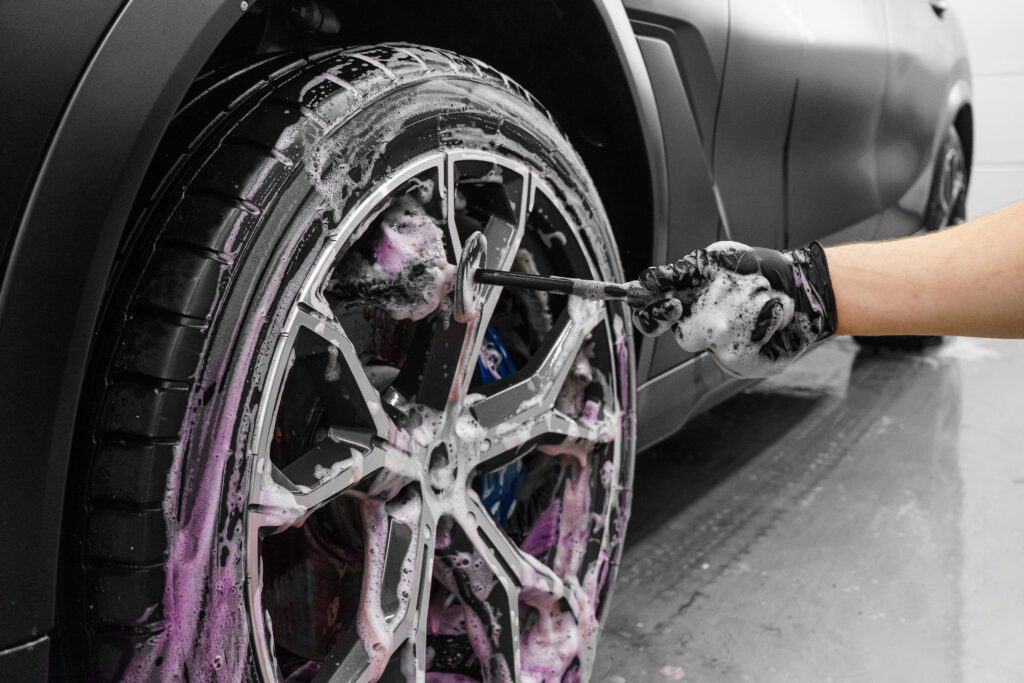 A detailer uses a tire brush to clean between the spokes of a wheel.