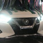 Tire Brushes Cleaning the Wheels of a White Sedan in a Car Wash Tunnel