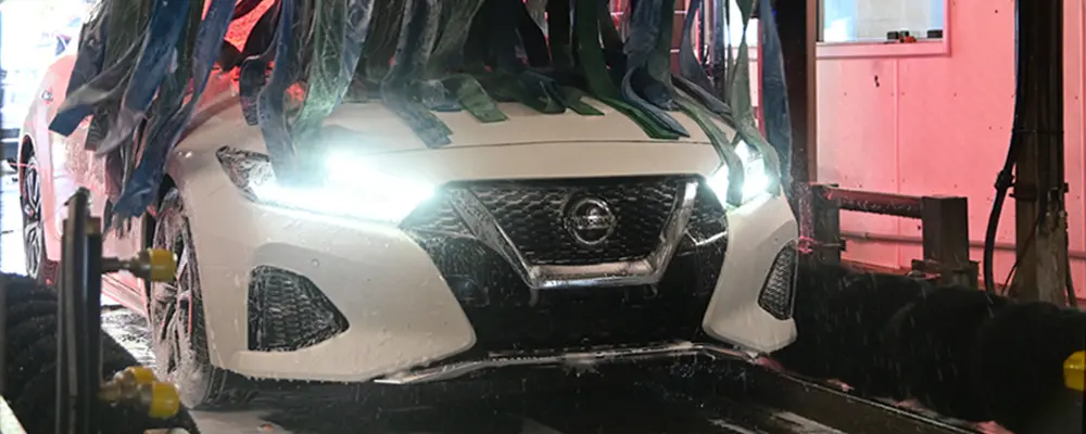 Tire Brushes Cleaning the Wheels of a White Sedan in a Car Wash Tunnel